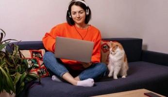 Mulher sentada no sofá com notebook no colo e gato ao lado